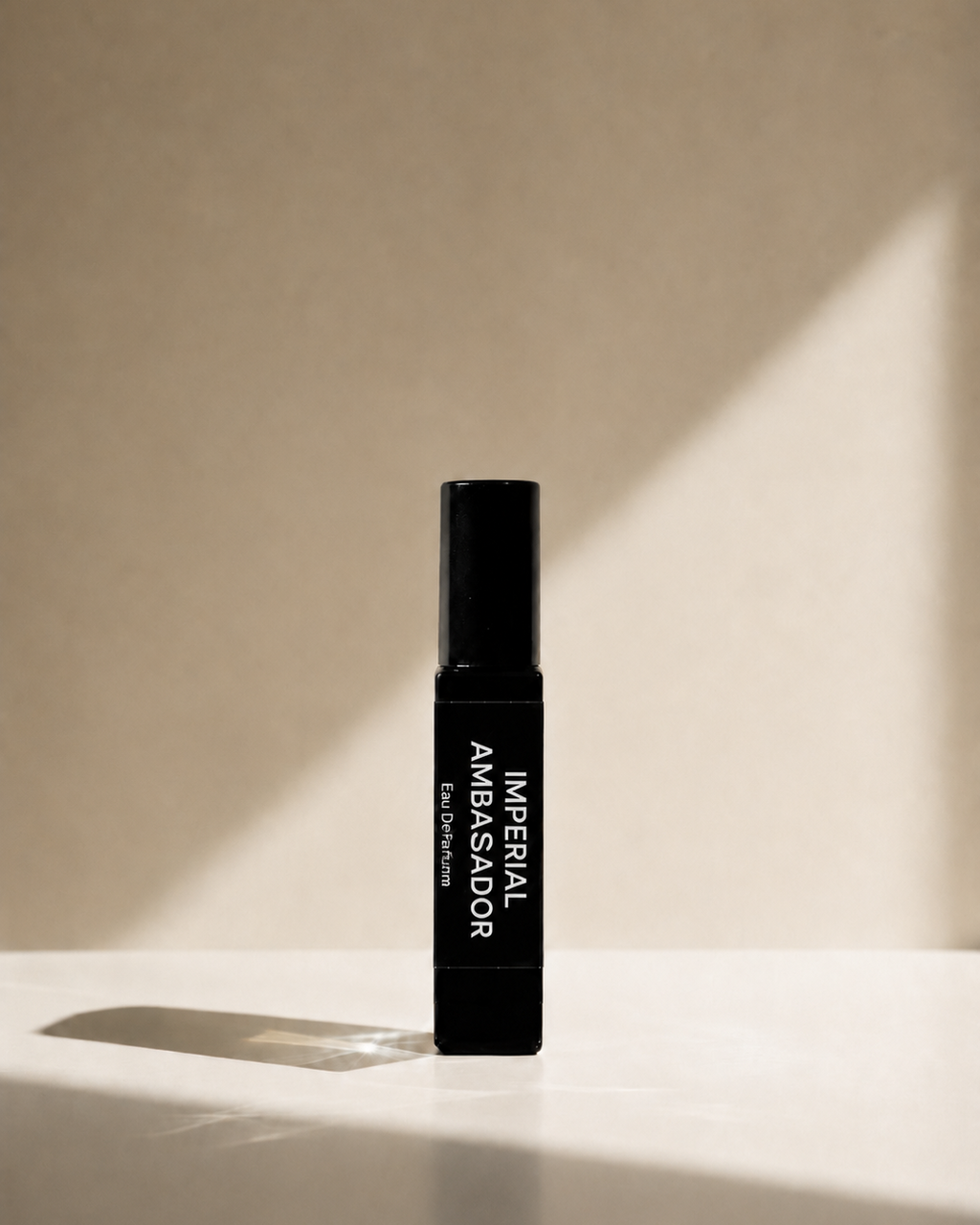 A black cylindrical cosmetic bottle labeled 'IMPERIAL AMBASSADOR' stands upright on a white surface against a beige wall, with dramatic diagonal sunlight casting shadows.