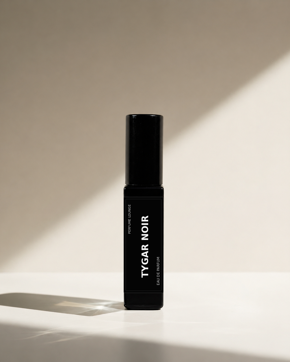 A black perfume labelled 'NOIR SANTALE' stands upright on a white surface against a beige wall, with dramatic diagonal sunlight casting shadows.
